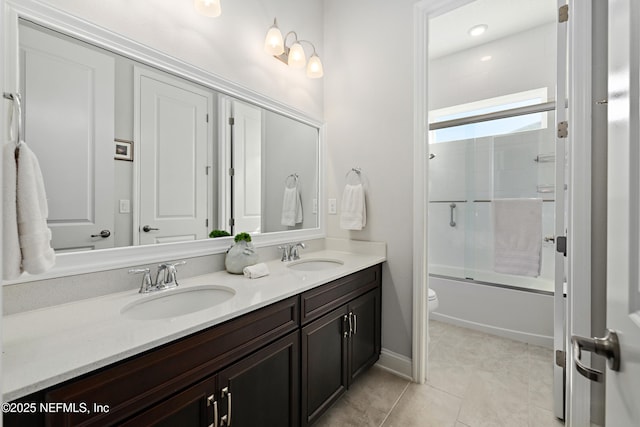 bathroom with double vanity, toilet, bath / shower combo with glass door, and a sink