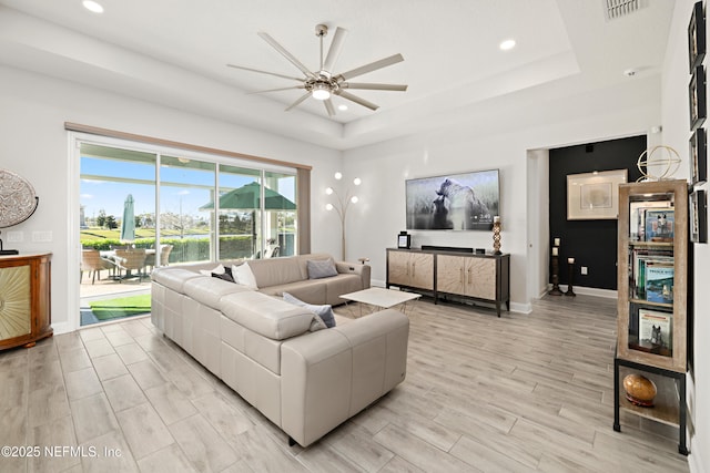 living room featuring a tray ceiling, light wood-style flooring, baseboards, and visible vents