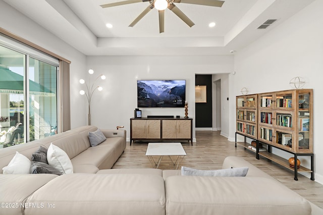 living room featuring a tray ceiling, baseboards, visible vents, and light wood finished floors