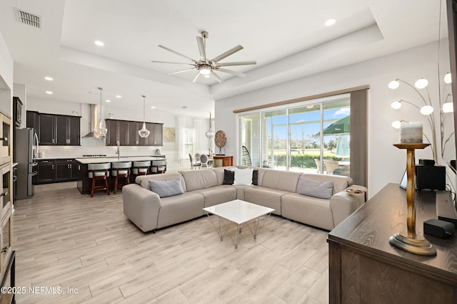 living room with light wood-style floors, a tray ceiling, a healthy amount of sunlight, and visible vents