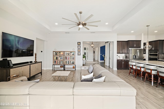 living area with recessed lighting, light wood-type flooring, a raised ceiling, and a ceiling fan