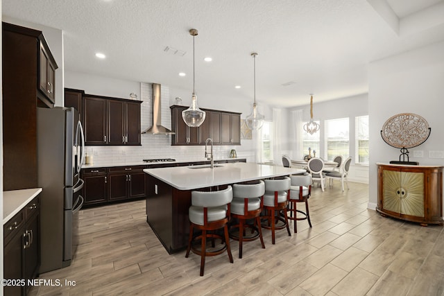 kitchen with backsplash, freestanding refrigerator, gas stovetop, wall chimney exhaust hood, and a sink