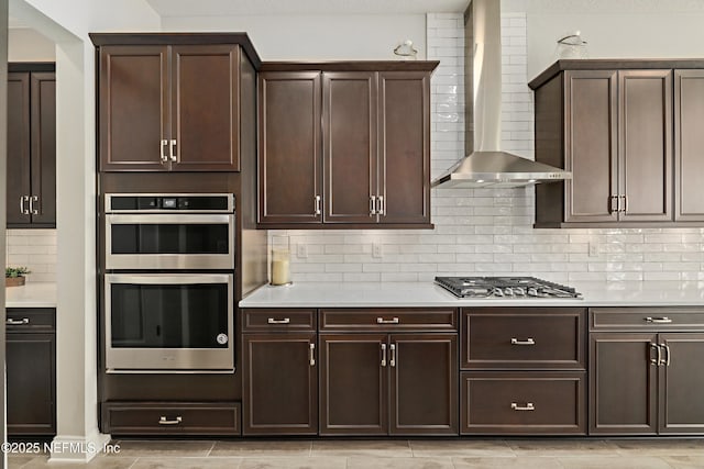 kitchen with dark brown cabinetry, appliances with stainless steel finishes, wall chimney exhaust hood, and light countertops