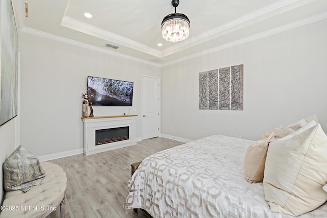 bedroom with a raised ceiling, light wood-style floors, ornamental molding, and a fireplace