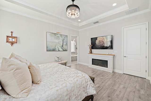 bedroom with visible vents, light wood-type flooring, a raised ceiling, and a glass covered fireplace