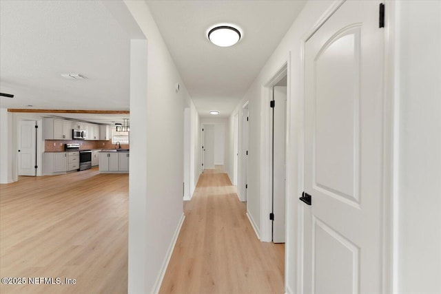 hall featuring light wood finished floors, a sink, visible vents, and baseboards