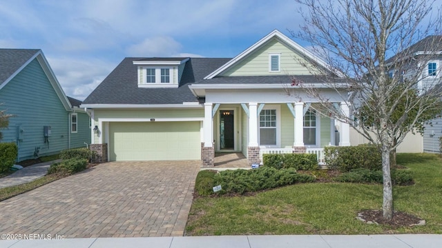 view of front facade featuring brick siding, roof with shingles, decorative driveway, a porch, and a front yard