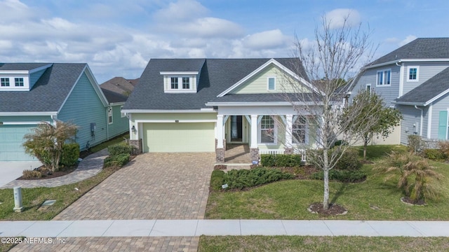 view of front of property with decorative driveway, a porch, a shingled roof, a garage, and a front lawn