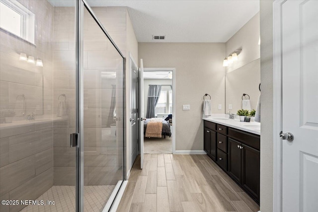 ensuite bathroom featuring double vanity, a stall shower, wood finished floors, ensuite bath, and a sink