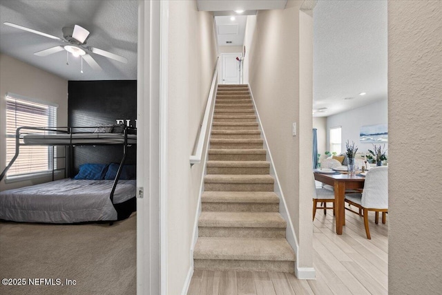 staircase with baseboards, wood finished floors, a textured wall, a textured ceiling, and a ceiling fan