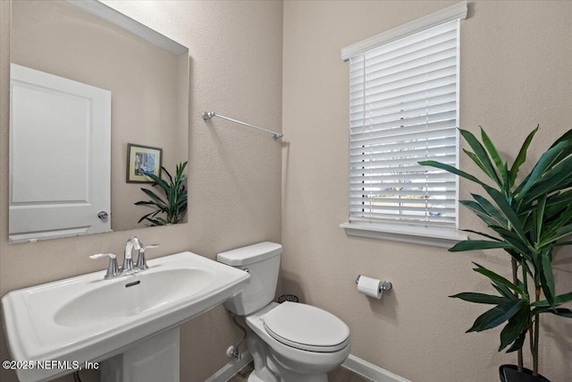 half bath featuring toilet, baseboards, and a sink