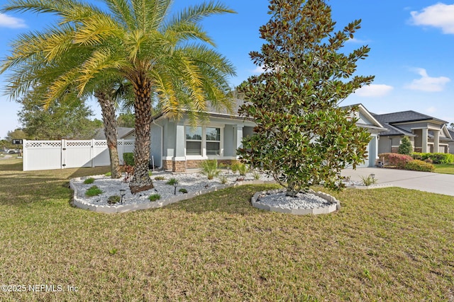 obstructed view of property featuring driveway, a garage, stone siding, fence, and a front yard