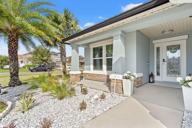 entrance to property featuring covered porch, stone siding, and stucco siding