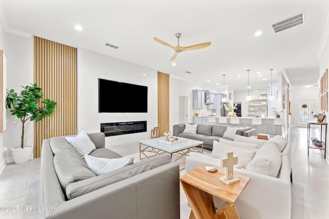 living room with a ceiling fan, visible vents, recessed lighting, a glass covered fireplace, and crown molding