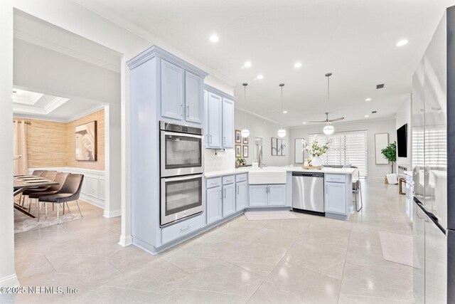 kitchen with a peninsula, a sink, stainless steel appliances, light countertops, and crown molding