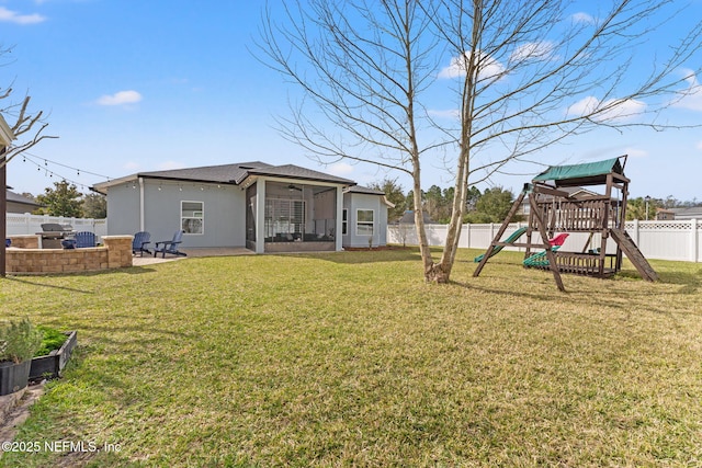 back of property with stucco siding, a fenced backyard, a playground, a yard, and a patio area