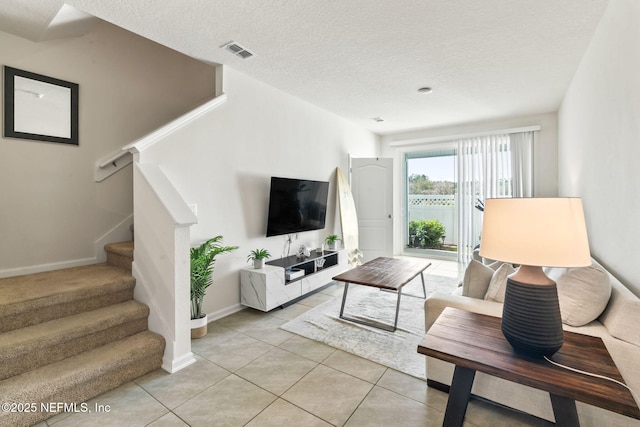 living room featuring light tile patterned floors, stairway, a textured ceiling, and visible vents