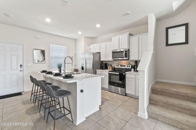 kitchen with a breakfast bar, a sink, white cabinetry, appliances with stainless steel finishes, and a center island with sink