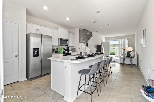 kitchen featuring light tile patterned floors, a center island with sink, white cabinets, stainless steel appliances, and light countertops