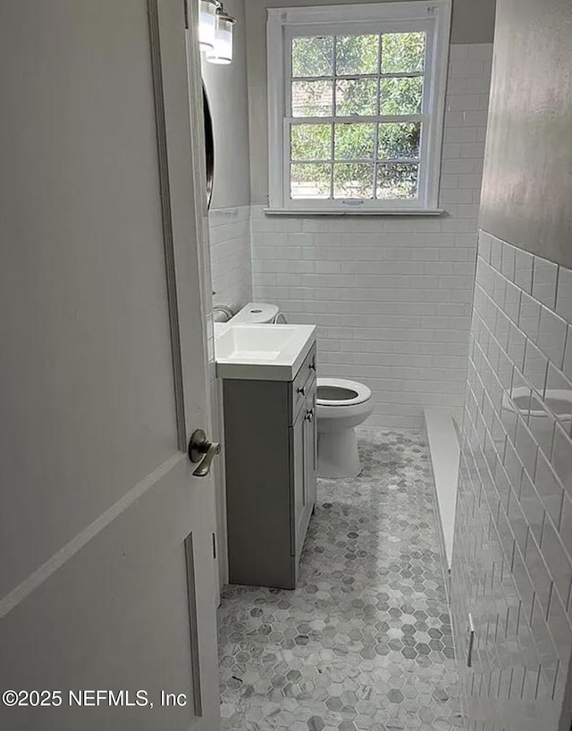 bathroom with toilet, vanity, and tile walls