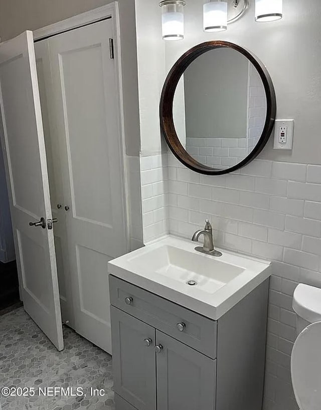 bathroom with toilet, vanity, and tile walls