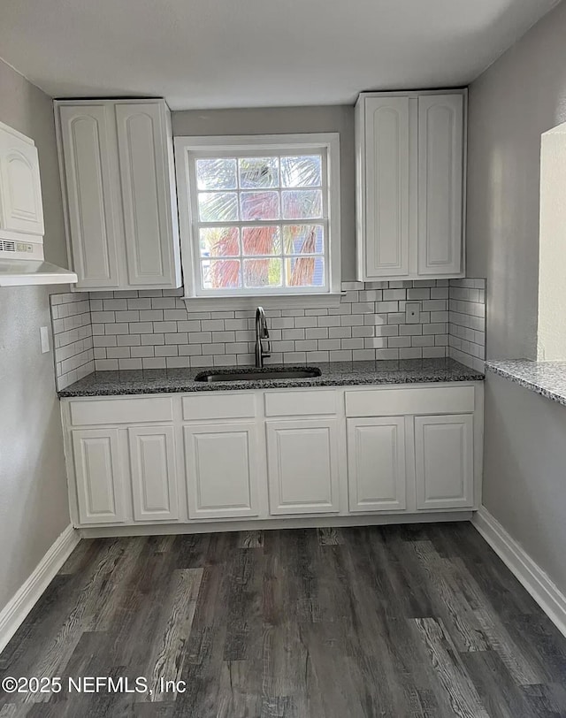 kitchen with dark stone countertops, dark wood-style flooring, tasteful backsplash, and a sink