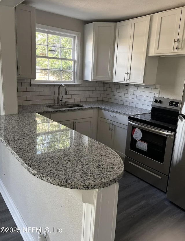 kitchen with dark wood-style flooring, decorative backsplash, white cabinets, stainless steel range with electric cooktop, and a sink