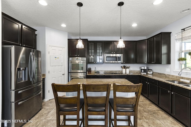 kitchen featuring a kitchen island, light stone counters, appliances with stainless steel finishes, hanging light fixtures, and a sink