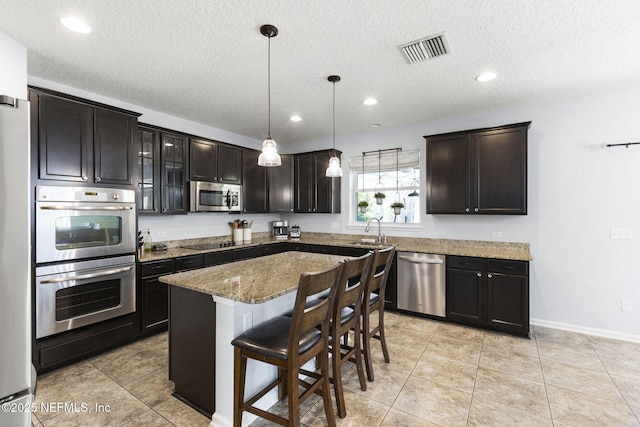 kitchen featuring visible vents, light stone counters, a kitchen breakfast bar, a center island, and appliances with stainless steel finishes