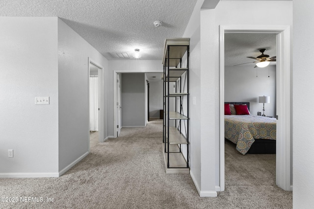 hall with baseboards, carpet floors, and a textured ceiling