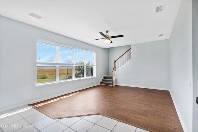 spare room with ceiling fan, stairs, visible vents, and baseboards