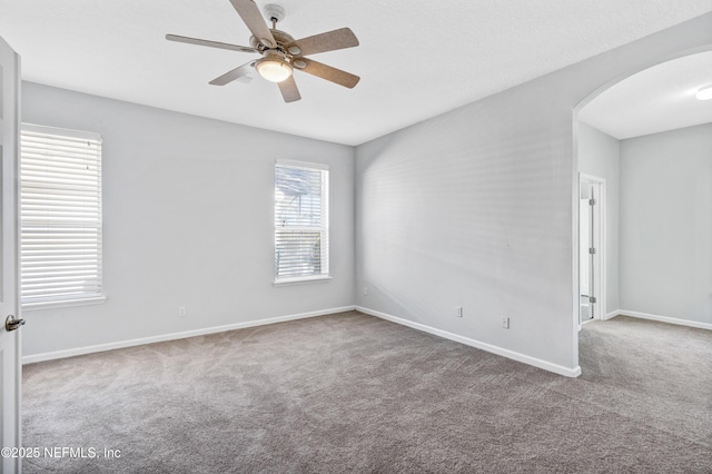 carpeted empty room featuring arched walkways, ceiling fan, and baseboards