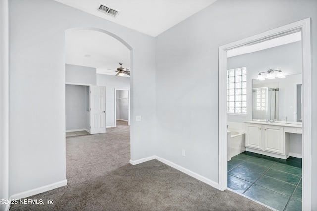 hallway featuring arched walkways, visible vents, dark carpet, and baseboards