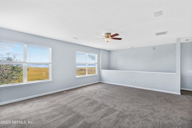 carpeted empty room featuring a ceiling fan, visible vents, a textured ceiling, and baseboards