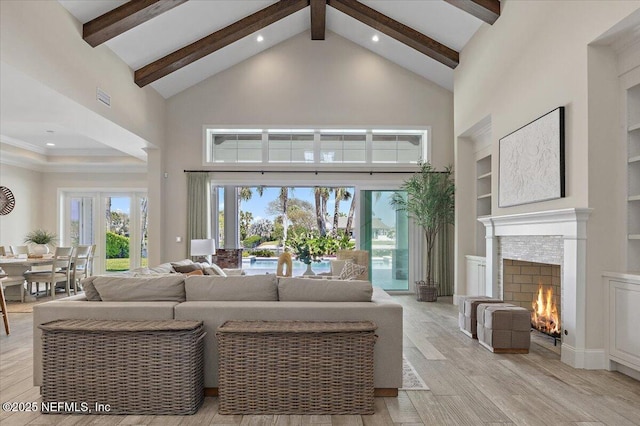 living area with light wood-type flooring, beam ceiling, a lit fireplace, and high vaulted ceiling