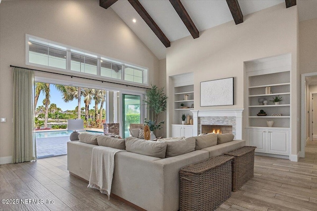 living room with baseboards, high vaulted ceiling, beam ceiling, a warm lit fireplace, and light wood-type flooring