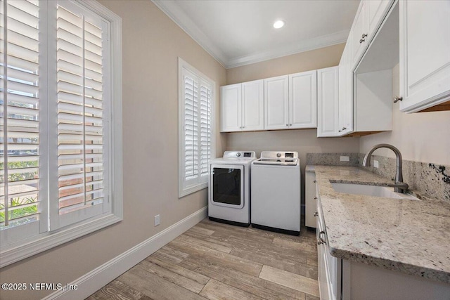 clothes washing area with light wood finished floors, washing machine and clothes dryer, cabinet space, ornamental molding, and a sink