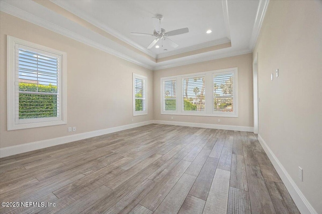 unfurnished room with baseboards, light wood-style flooring, ceiling fan, crown molding, and a raised ceiling