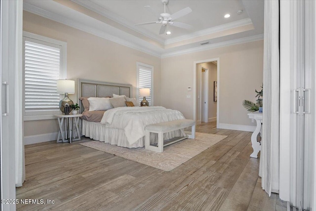 bedroom featuring a raised ceiling, crown molding, light wood-type flooring, and baseboards