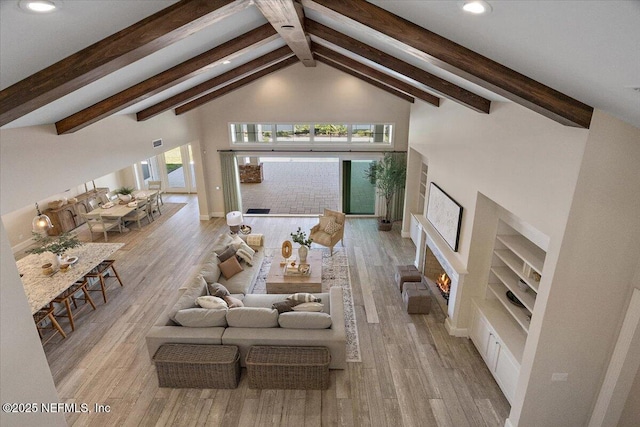 living room with beam ceiling, recessed lighting, a warm lit fireplace, wood finished floors, and high vaulted ceiling