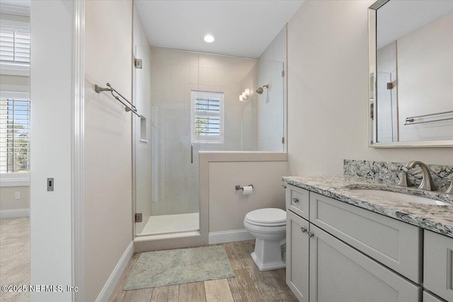 bathroom with toilet, a stall shower, wood finished floors, baseboards, and vanity