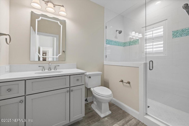 bathroom with vanity, wood finished floors, baseboards, a stall shower, and toilet