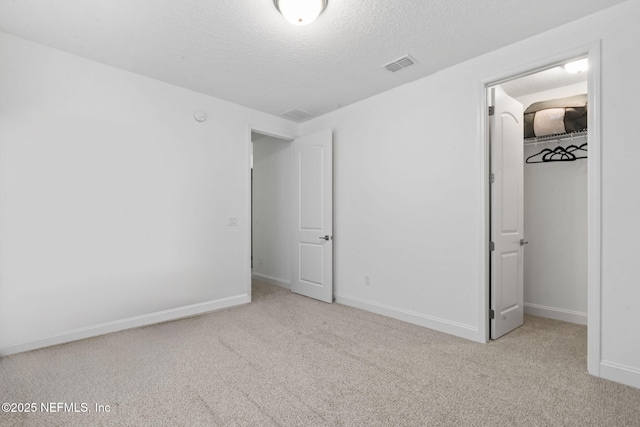 unfurnished bedroom with carpet floors, a walk in closet, visible vents, a textured ceiling, and baseboards