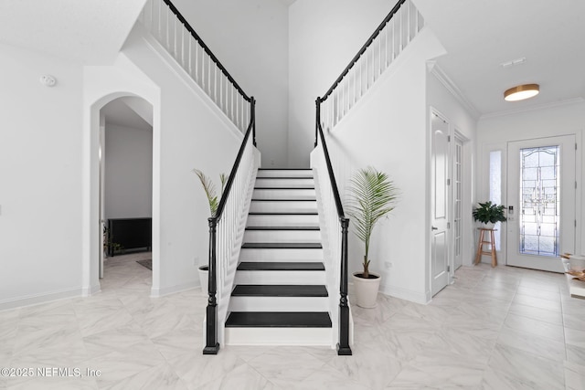 entrance foyer featuring ornamental molding, arched walkways, stairway, and baseboards