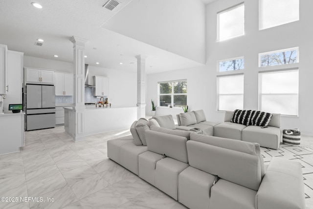 living area featuring visible vents, a towering ceiling, marble finish floor, ornate columns, and recessed lighting