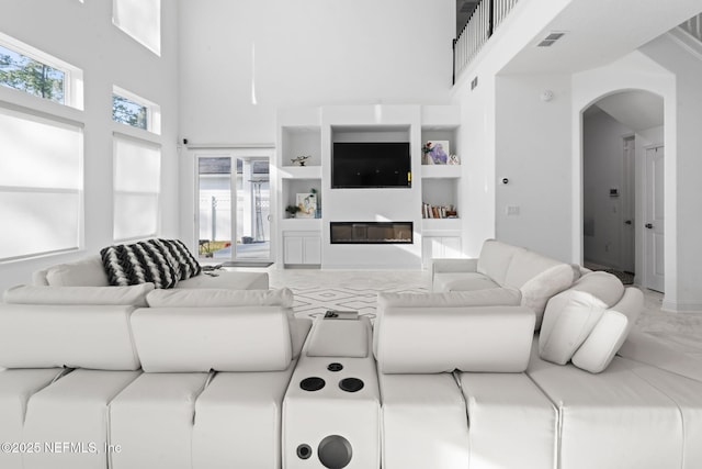 living area featuring arched walkways, a glass covered fireplace, visible vents, and a towering ceiling