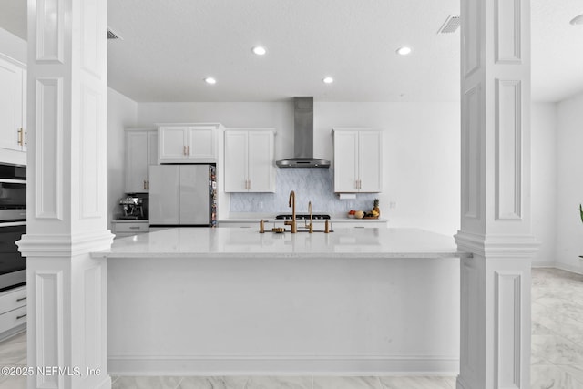 kitchen with decorative columns, visible vents, white cabinets, wall chimney exhaust hood, and appliances with stainless steel finishes