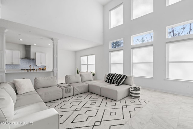 living area with marble finish floor, recessed lighting, ornate columns, a towering ceiling, and baseboards