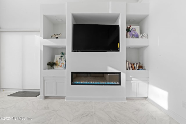 living room with built in shelves, a glass covered fireplace, marble finish floor, and baseboards