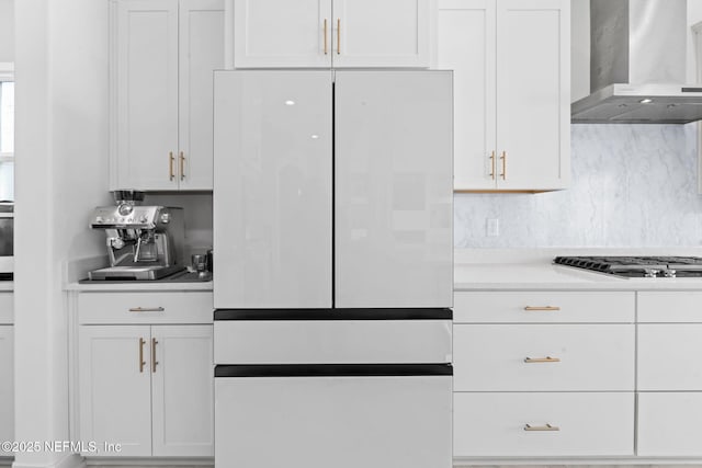 kitchen with freestanding refrigerator, light countertops, wall chimney range hood, white cabinetry, and gas cooktop